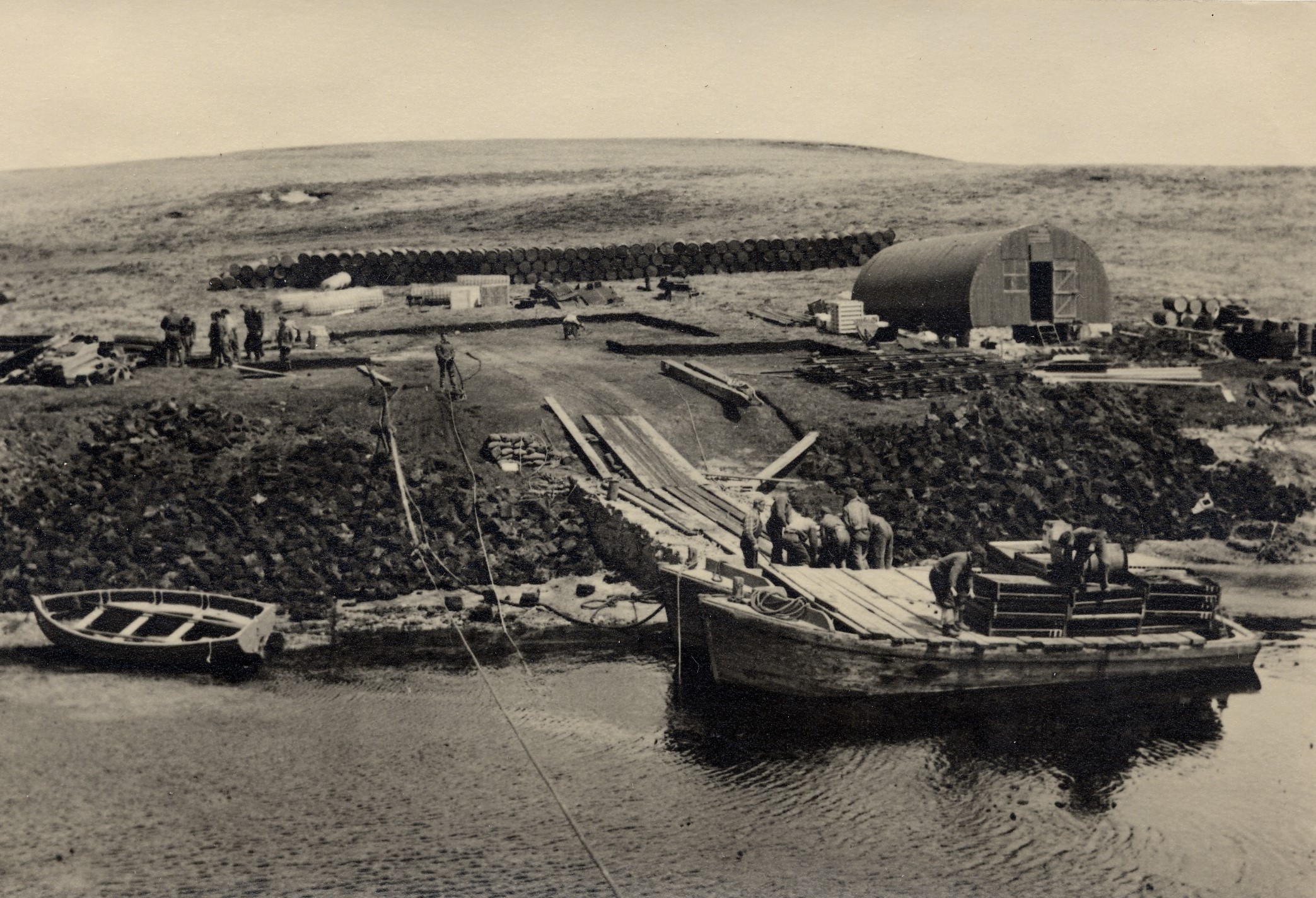 FC 007 0063. Ajax Bay under construction. Scows at jetty. Drums and Nissen Hut in background 1949